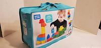 Photo of closed turquoise Mega Bloks carrying bag showing product label with images of blocks and child playing.