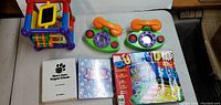 Photo of two toy rotary phones, a colorful plastic activity cube, two children’s books, and a Quiz Kids board game box.