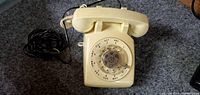 Ivory colored rotary dial desk telephone with handset and cord, showing dial letters and numbers.