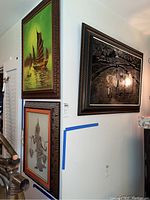 Wall corner with three framed Asian art pieces: a junk boat painting, a black and white print of a figure, and a large framed rice paddy scene
