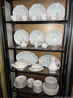 Full shelving display showing entire china set with all plates, bowls, cups, saucers, and serveware pieces.