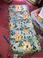 Full view of one floral patterned outdoor bench cushion on floor, shows size and pattern clearly.