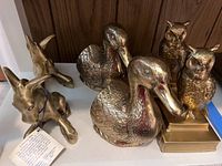 Brass animal bookends including two ducks, two owls on bases, and a donkey figurine on shelf