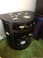 Front and top view showing the black lacquer barrel cabinet with detailed floral inlay and brass handles and knobs.