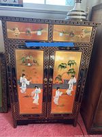 Front view of lacquer chest showing painted low reliefs of Chinese ladies and children in traditional attire with a scenic backdrop. Metal ring handles on drawers and doors.