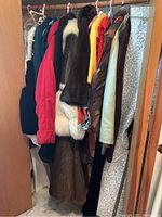 Photo showing an assortment of women's coats, fur coats, dresses, vests, and winter coats hanging in a closet on hangers, sizes approximately 18/20, L or XL.
