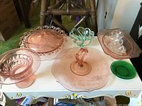 Photo of seven pieces of depression glass on a table showing various pink glassware items with one green and one teal piece