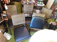 Five folding dining chairs with cane backs and black cushioned seats arranged on a green carpet in a room with other furniture and items.