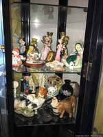 Display cabinet with porcelain figurines, brass candleholders, decorative lighthouses, and animal figurines.