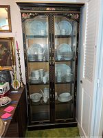 Full front view of black Asian themed cabinet with glass doors displaying white dishware inside.