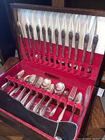 Photo of silverplate cutlery knives held vertically in red velvet slots inside wooden box.