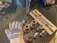 Overview of silver candlesticks, salt and pepper shakers, carving set, flute vase and oven glove on glass table