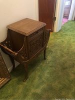 Full view of telephone stand showing top surface, side magazine holders and carved legs on green carpet