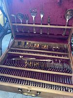 Wooden storage box open showing velvet-lined interior with trays of flatware and serving utensils
