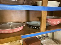 Shelf display of vintage Pyrex dishes with distinct floral patterns and glass lids