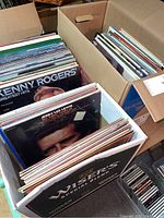 Three cardboard boxes filled with vinyl LP albums seen from above, showing record covers from Kenny Rogers Greatest Hits and Jerry Lee Lewis The Killer Rocks On.