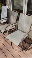 Two metal framed swivel patio chairs with light brown mesh seats and backs on a wooden deck. Chairs have circular bases for swivel functionality.