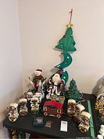 Full view of various Christmas decorations including ceramic tree, Santa figures, snowmen, ceramic boots, carousel horse set with red base.