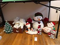 Wide shot showing ceramic Christmas tree, large snowman, stuffed angel and Santa, mice, and Santa in tub figures arranged on floor.