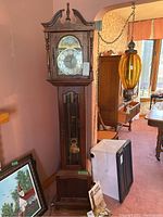 Front view of tall wooden grandfather clock with clock face, weights visible behind glass door, and extra pendulum included.