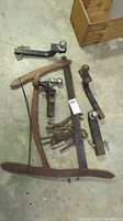 Overview of vintage hand tools on basement floor including frame saw, five tow balls with hitches, and a stack of old wrenches.