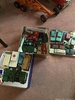Displayed tin containers filled with assorted vintage die cast metal toy vehicles including military, race cars, ambulances, and tractors.