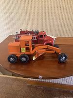 Front and side view of red fire truck and orange grader on wooden table