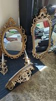 Two ornate framed mirrors standing on floor along with matching hanging shelf and candle holders laid out around them, showing overall condition and design.