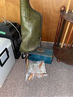 Fishing rod in green protective case, with tackle box and plastic bag of tackle on floor next to it.