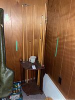 Wide view of corner wooden pool cue rack holding multiple pool cues, some leaning on the wall next to it.
