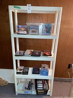 Front view of the white resin shelving unit with CDs, DVDs, cassette tapes, and bins containing additional items.