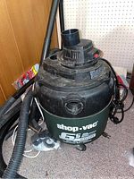 Photo of the Shop Vac unit showing the 6.5 gallon capacity label, hose attachments, and cassette wheels base.