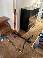 Photo of two red Rockwater Designs trekking poles leaning against wall next to black metal bed support frame on carpeted floor.