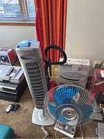 Photo showing all items including the red Dirt Devil vacuum, silver tower fan, blue smaller fan, and boxed iRobot Roomba.