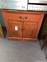 Front view of wood cabinet with drawer and double doors, showing details of handles and wood finish.