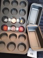 Four-piece set of baking pans showing two muffin pans (12 cup and 6 cup) and two loaf pans, all in dark gray non-stick metal.