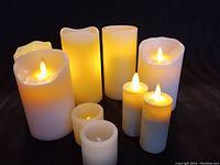 Eight off-white battery operated faux candles with realistic flame LEDs arranged in a group on a dark surface.