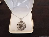 Necklace displayed in a white satin-lined jewelry box showing round pendant with intricate Celtic knot design.