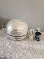 Photo showing the Sparoom aroma diffuser in silver and white with two essential oils beside it.