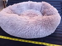 Side angle showing the fluffy taupe donut style calming dog bed with measuring tape alongside for size reference, showing approximately 29 inches diameter.