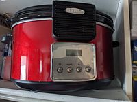 Front view of a red Rival crockpot with black top and base, showing the digital control panel with buttons and display.