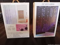 Two West & Arrow LED curtain lights boxes, one opened and one sealed, showing product packaging with night usage image and lighting modes.