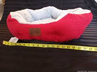 Red and grey pet bed with a tape measure showing approximately 18 inches in length.