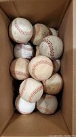Top-down view of a box containing 14 used baseballs with red stitching, some with dirt and wear marks.