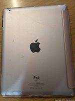 Back of iPad Mini showing metallic surface, Apple logo, and part of pink case attached.