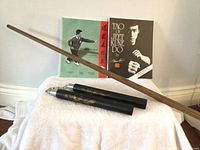 Photo showing a 6-foot oak bo staff resting on two martial arts books, one titled 'Tao of Jeet Kune Do' and another Chinese instructional book with a martial artist on the cover.