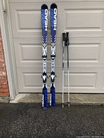 Pair of Head skis standing upright against a garage door with a pair of Gabel Rival ski poles to the right