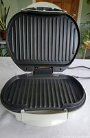 Open panini press showing ribbed non-stick grilling plates inside, clean and ready for use