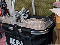 Black picnic basket with silver metal handles, wrapped in cellophane and topped with a black and white striped bow. Photos show details of basket and wrapping.