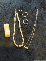 Overview photo showing all jewellery pieces in the lot: bead necklace with bead earrings, infinity loop necklace, hoop earrings, and mesh bracelet.